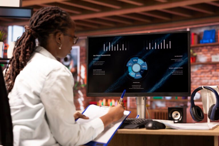 Woman looking at sales statistics on computer, taking notes